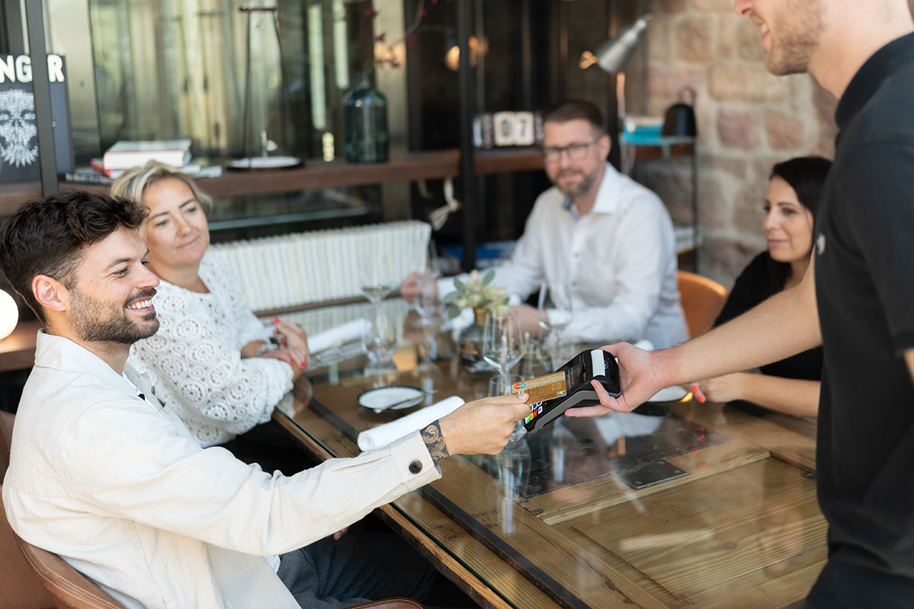 Eine Gruppe Menschen sitzt im Restaurant am Tisch und bezahlt mit Karte